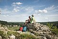 Wanderpärchen an den 12 Apostel bei Solnhofen Zwei Wanderer sitzen auf einem Felsen und blicken auf bewaldete Hügel unter blauem Himmel mit Wolken.