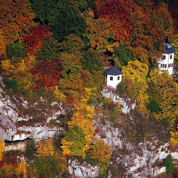Das Gebiet der Tropfsteinhöhle von oben fotografiert. Die zwei Gebäude blitzen durch das bunte Herbstkleid des Waldes durch.