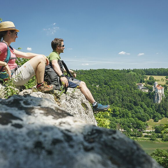 Der Aussichtspunkt am Altmühltal-Panoramaweg bei Riedenburg Auf dem Aussichtspunkt gegenüber Burg Prunn sitzen im Vordergrund ein Pärchen mit Blick ins Tal gerichtet.